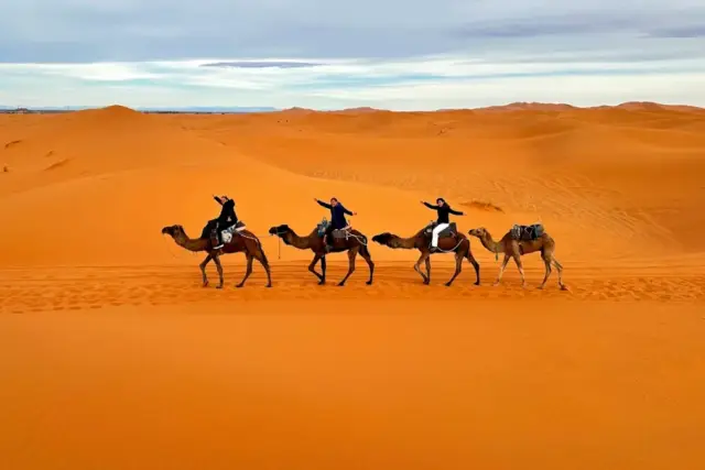 Viajeros en fila sobre dromedarios atravesando las dunas de Erg Chebbi, en Merzouga, con el sol bajo
