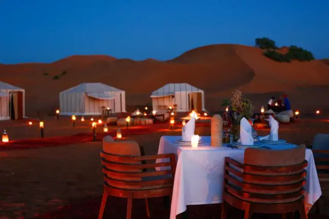 Mesa para dos con farolitos encendidos sobre las dunas de Merzouga al anochecer